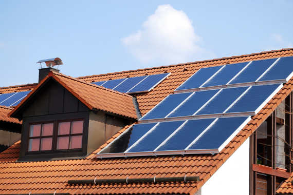 Solar panels being installed on the tiled roof of a residential home under a clear blue sky.