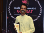 Founder of Jalark Solars, smiling and holding a trophy on stage with an awards banner in the background