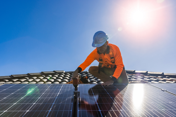 A certified technician installing a solar panel on a commercial roof, securing the module under a bright sun.