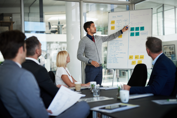 A business meeting where an executive is presenting a solar proposal to several clients around a conference table.