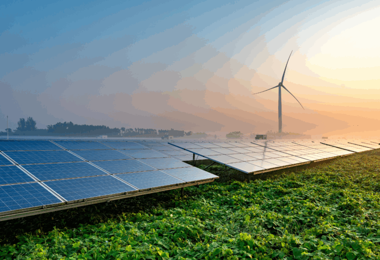 Solar panels and a large wind turbine standing together in a green, grassy field, symbolizing combined renewable energy generation.