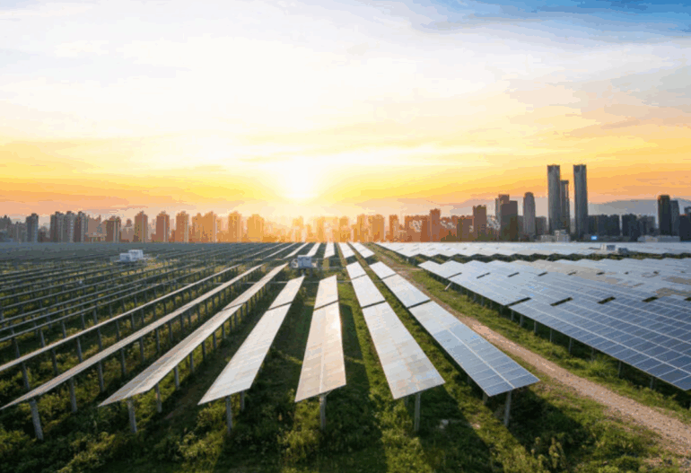 Expansive utility-scale solar farm with countless rows of panels, bathed in the light of a rising or setting sun, with a city visible in the distance.