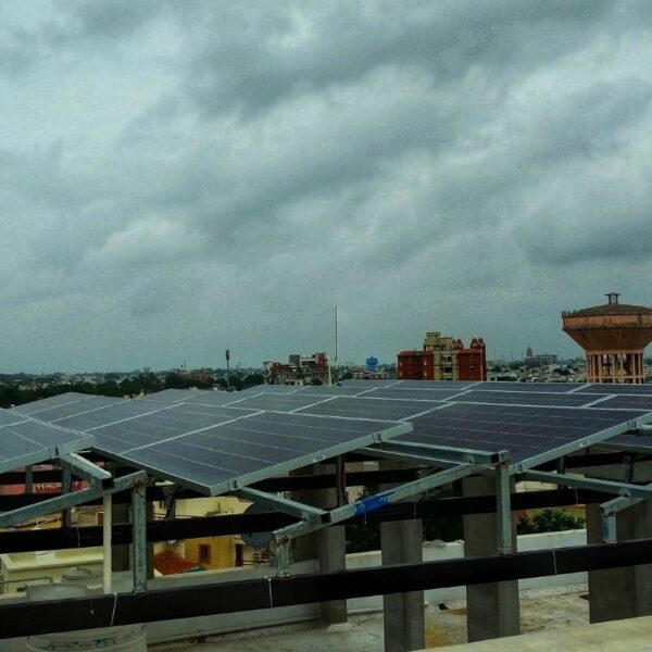 A large array of solar panels mounted on a building rooftop in an urban area under a cloudy sky.