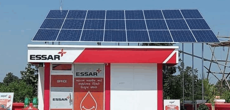 Solar panels installed over a red and white Essar office structure, with a blue sky background.