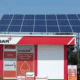 Solar panels installed over a red and white Essar office structure, with a blue sky background.
