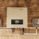 A central solar inverter mounted on a textured brick wall with visible wiring, likely for a commercial or large residential installation.